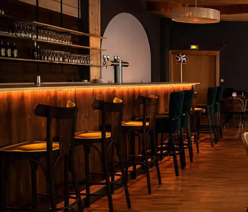 Comptoir en bois du Boleston souligné d'un bandeau lumineux ambre, tabourets alignés et verrerie sur les étagères